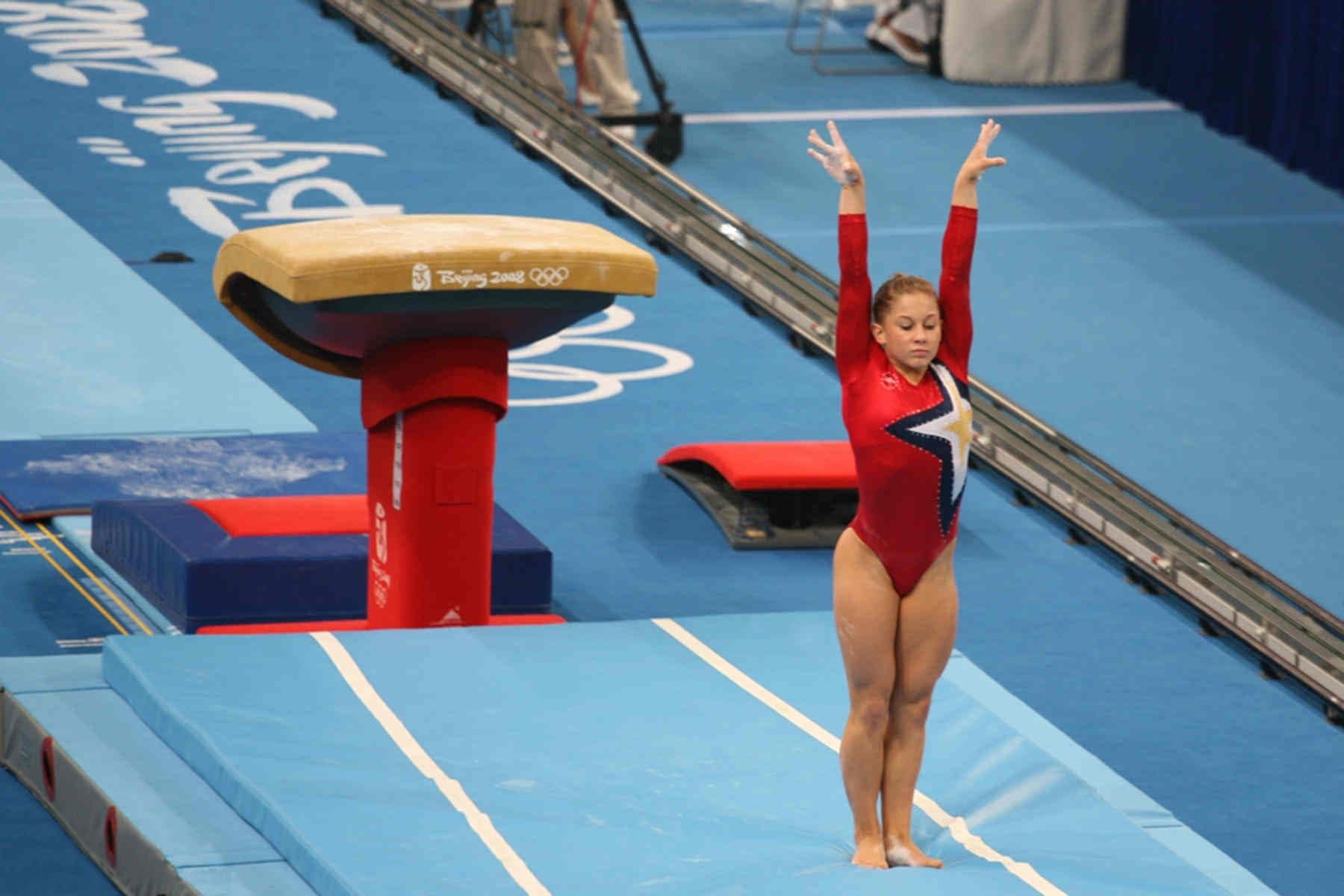 A USA gymnast sticking a vault landing with arms raised at the Olympics